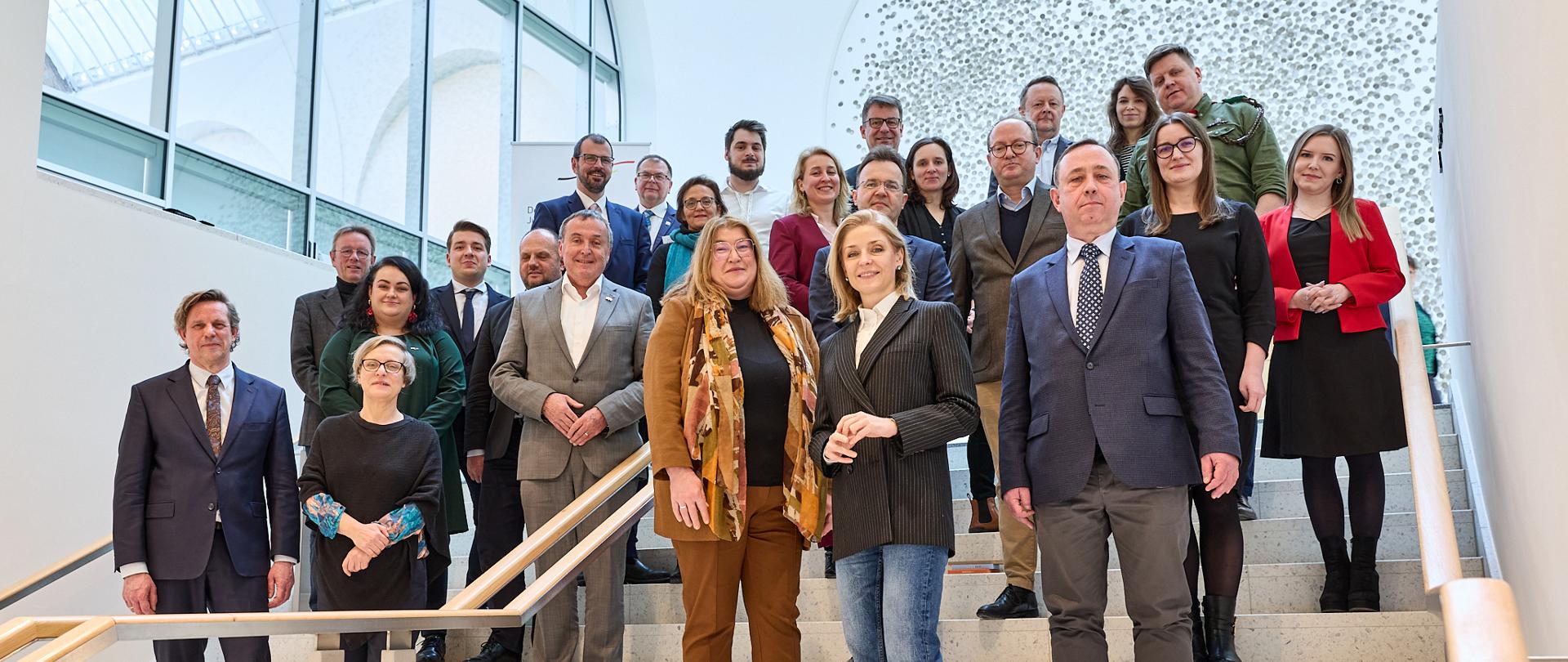 Zdjęcie zbiorowe na schodach stoi duża grupa ludzi i pozuje do zdjęcia