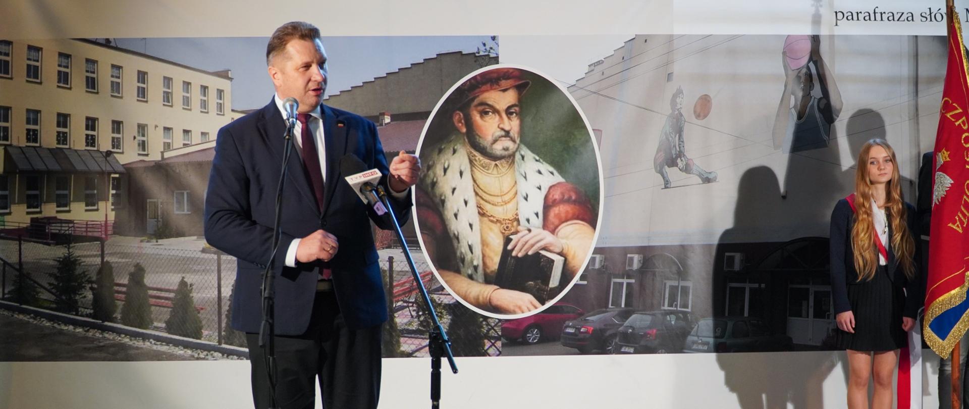 Minister Czarnek przemawia do mikrofonu, za nim baner szkoły ze zdjęciem Mikołaja Reja