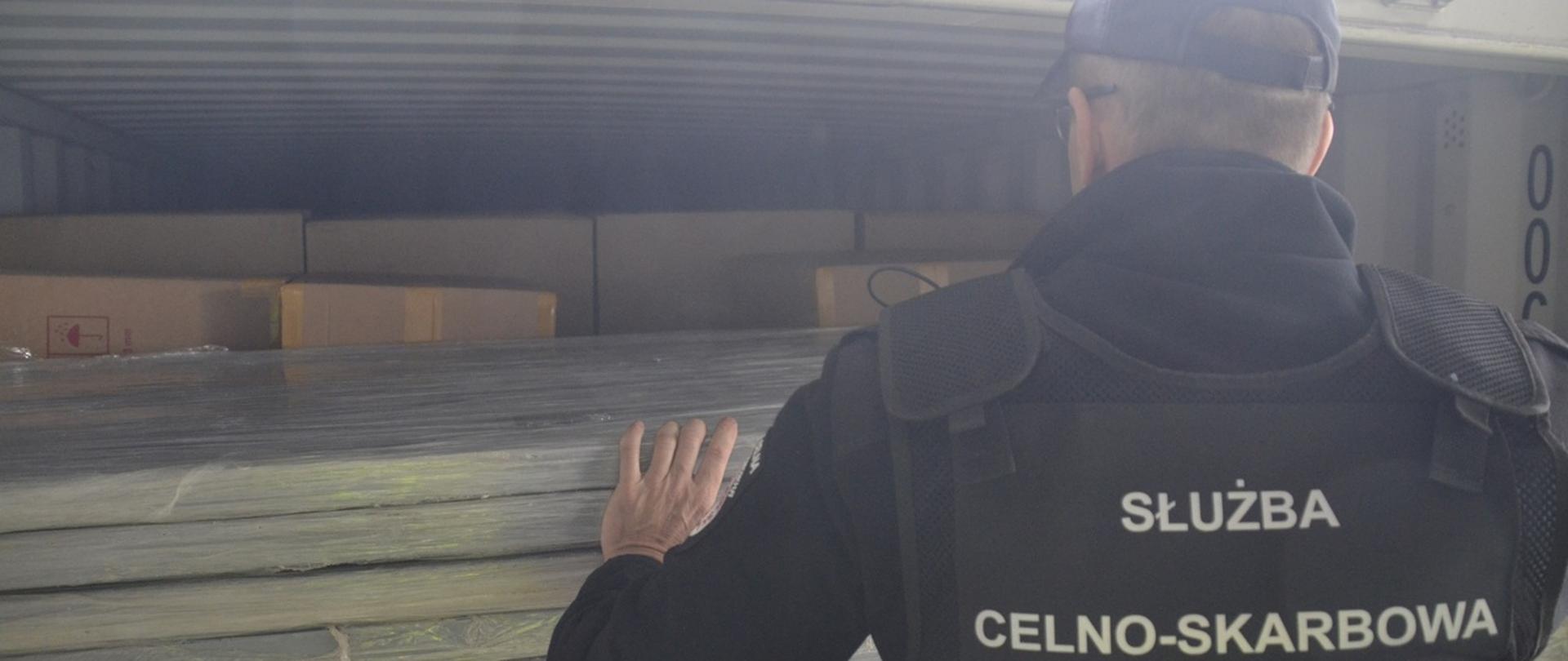 Funkcjonariusz KAS przed kontenerem wyładowanym drzwiami. W głębi kontenera pudła z nielegalnymi papierosami.