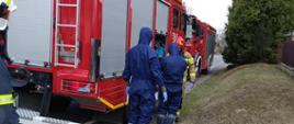 Ratownicy przygotowują się do pomocy w transporcie osoby do karetki pogotowia ubrani w kombinezony ochronne