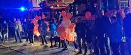 Rodzina i znajomi czekają na strażaków. W rękach trzymają balony oraz transparent.