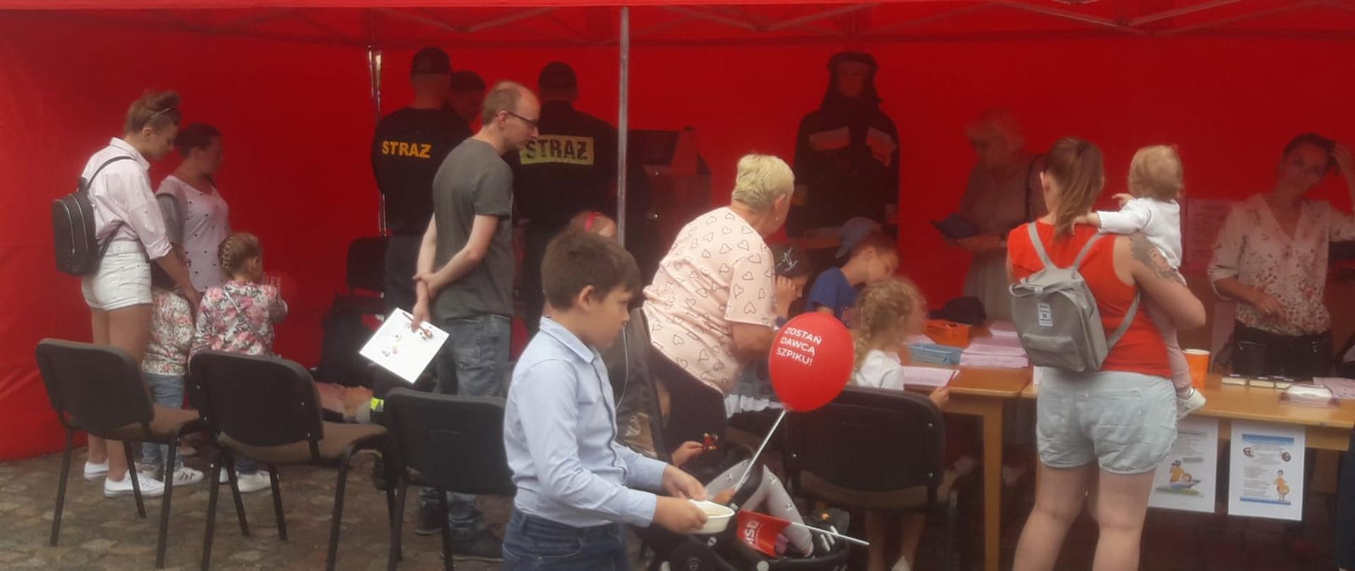 Zdjęcie przedstawia stoisko strażaków podczas dnia bezpieczeństwa. Na zdjęciu są ludzie odwiedzający stoisko.