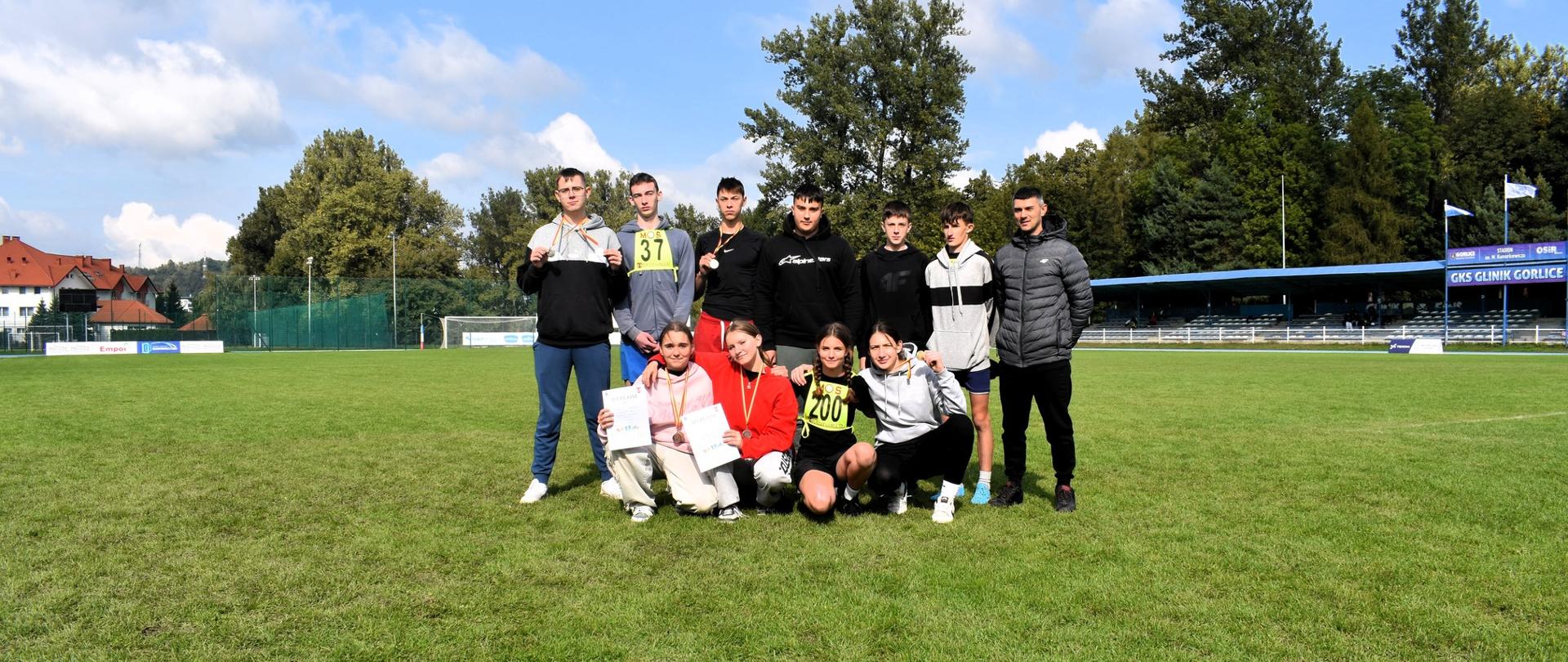 Grupowe zdjęcie medalistów na boisku sportowym.