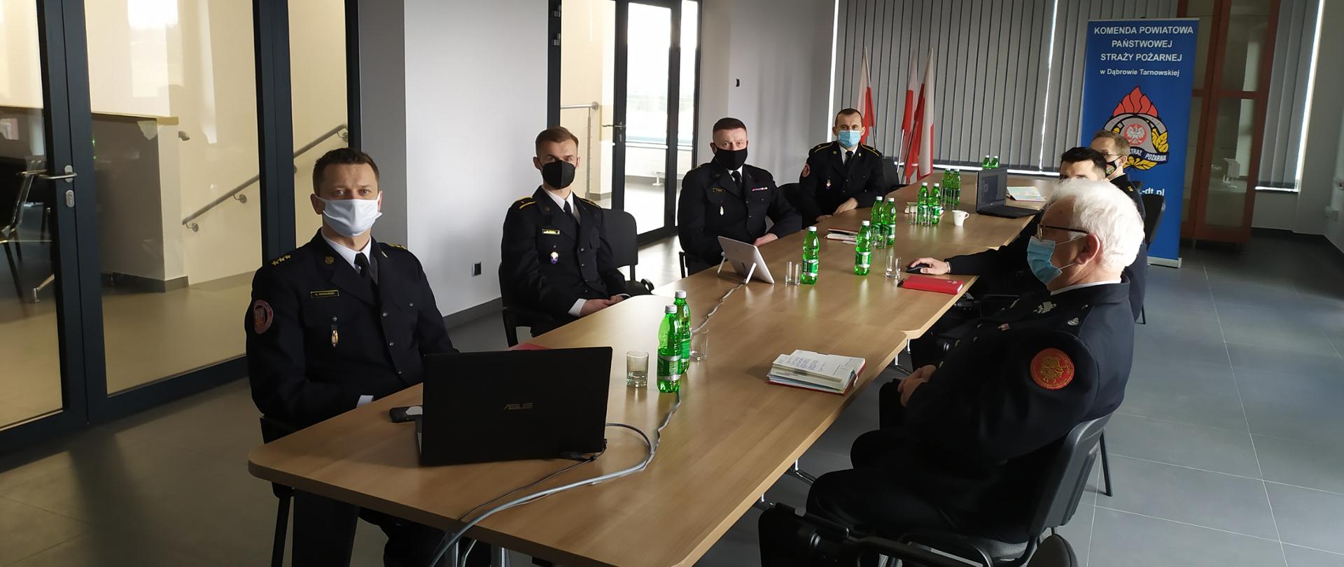 Na zdjęciu strażacy siedzą przy stole podczas narady