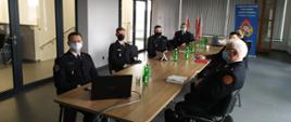 Na zdjęciu strażacy siedzą przy stole podczas narady