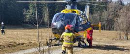 Strażak klęczy na jednym kolanie przed śmigłowcem LPR. 