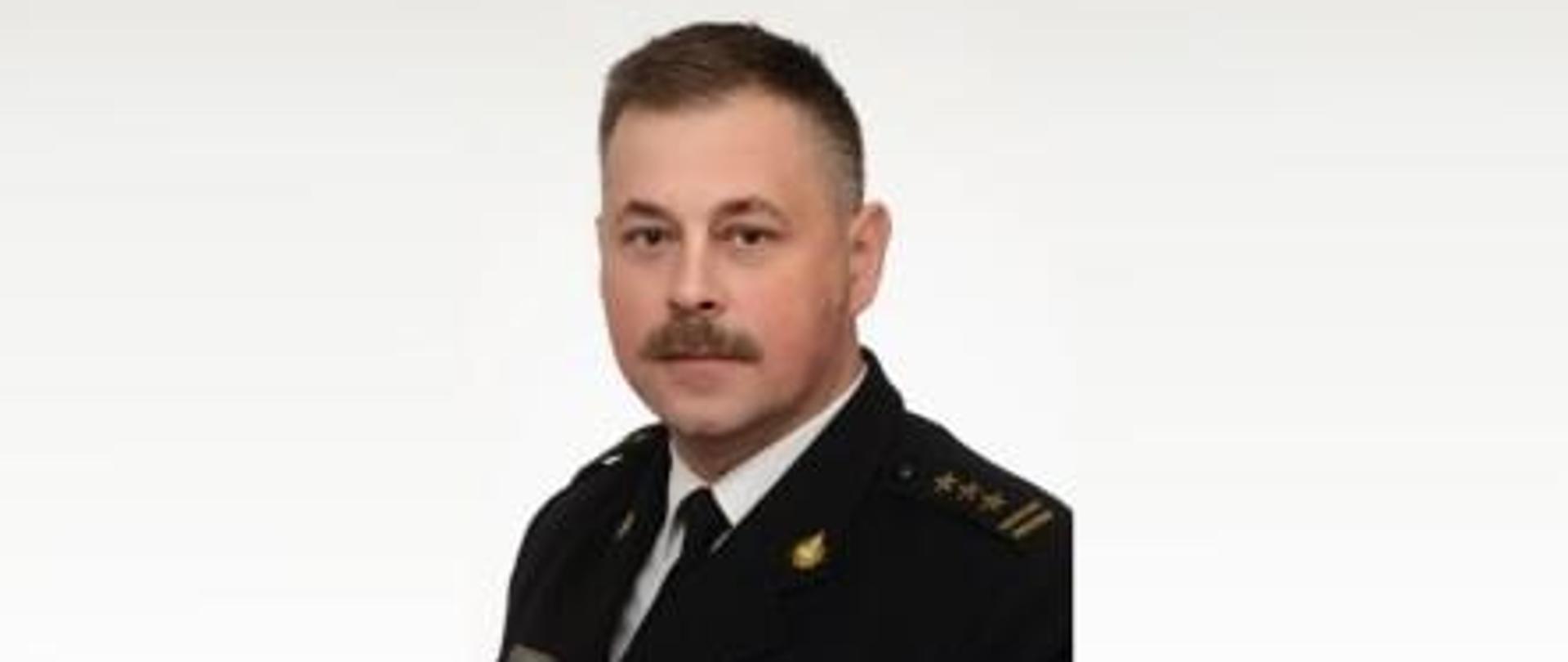 Zdjęcie przedstawia zdjęcie Zastępcy Komendanta Miejskiego Państwowej Straży Pożarnej st. bryg. Marcina Ziomka ubranego w mundur galowy. Zdjęcie wykonane na białym tle.