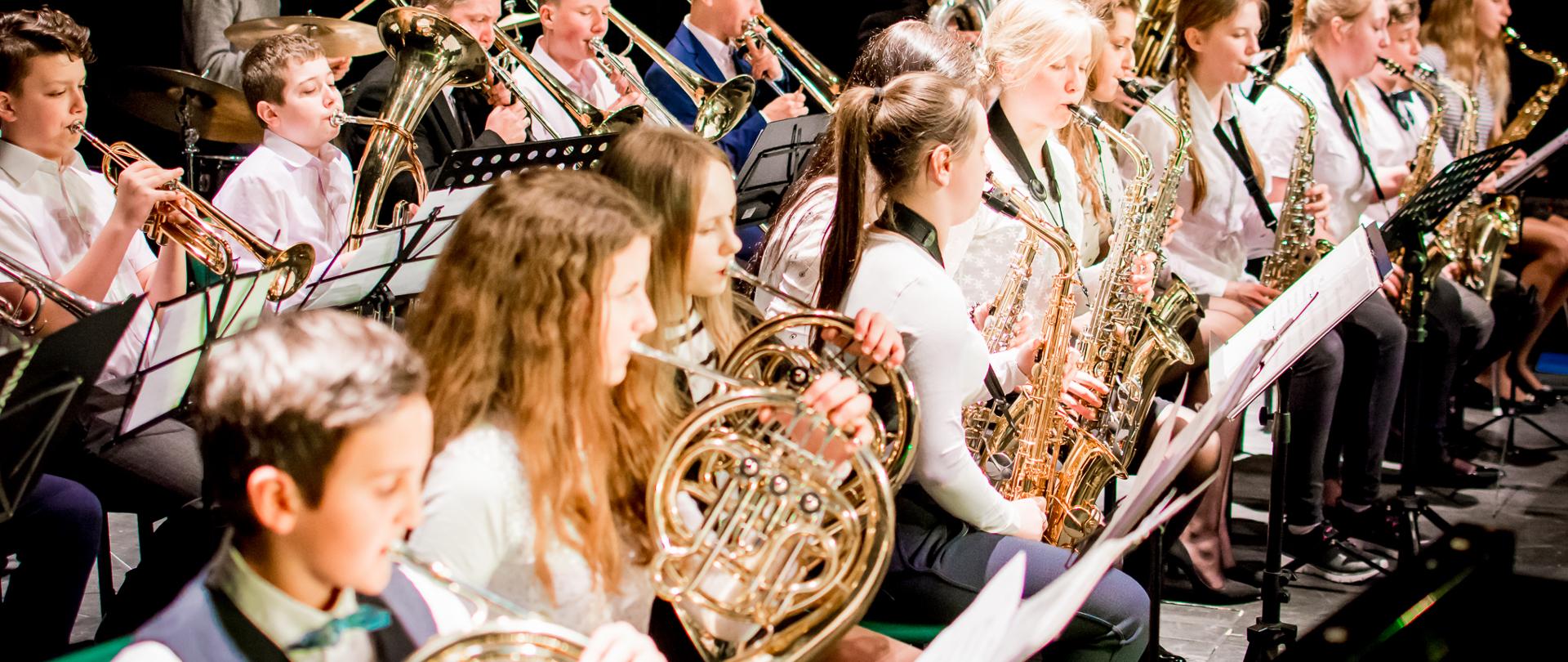 Uczniowie i absolwenci grający na instrumentach dętych i zestawie perkusyjnym podczas koncertu