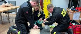 trzech strażaków w czasie egzaminu. Prowadzą czynności z zakresu kwalifikowanej pierwszej pomocy na manekinie