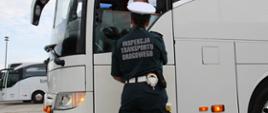 Kontrola autokaru turystycznego przed wyjazdem dzieci i młodzieży na letni wypoczynek. Inspektor mazowieckiej Inspekcji Transportu Drogowego pobiera od kierowcy wymagane dokumenty do kontroli.