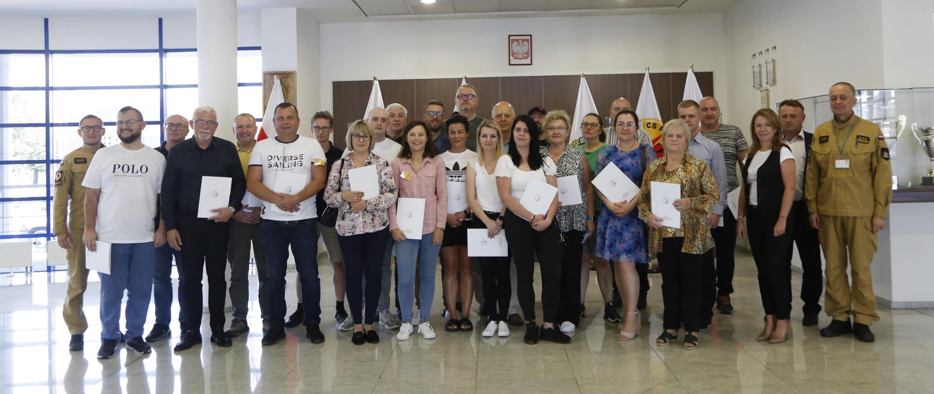 Grupowe zdjęcie uczestników szkolenia ppoż (25 osób) w towarzystwie dwóch funkcjonariuszy CS PSP oraz kobiety