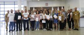 Grupowe zdjęcie uczestników szkolenia ppoż (25 osób) w towarzystwie dwóch funkcjonariuszy CS PSP oraz kobiety