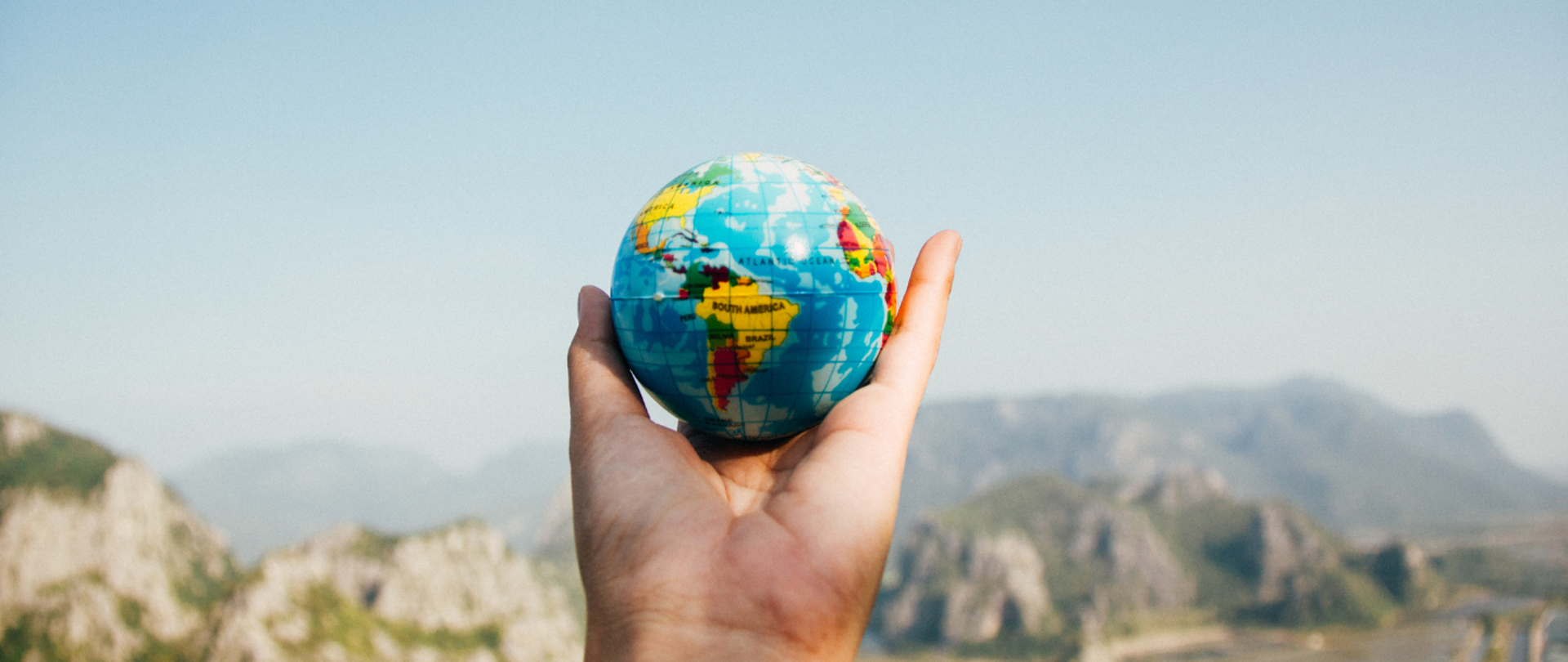 Ręka trzymająca mały globus na tle górskiego pejzażu