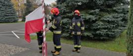 Przygotowanie do podniesienia flagi. Strażacy przypinają flagę do masztu.