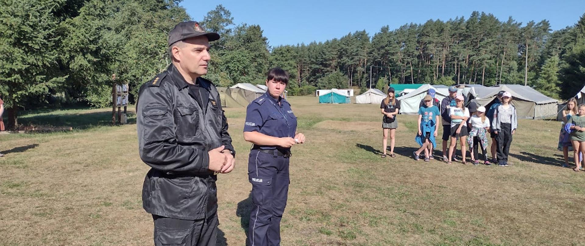 kapitan Mirosław Śledź z Komendy Powiatowej Państwowej Straży Pożarnej w Szczecinku ubrany w ubranie dowódczo sztabowe oraz aspirant Anna Matys z Komendy Powiatowej Policji w Szczecinku w mundurze policyjnym stoją przed harcerzami 
