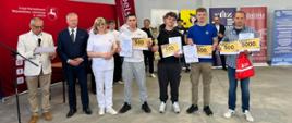 Grupowe zdjęcie laureatów z dyplomami i nagrodami oraz organizatorów na tle banerów.