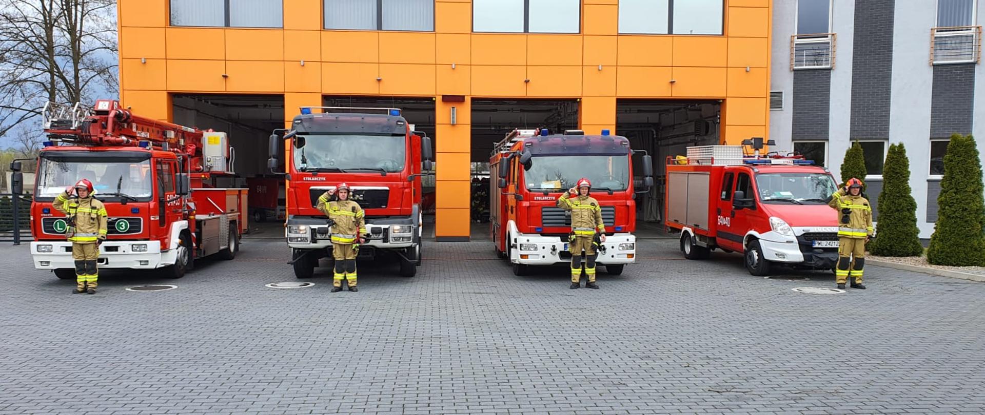 Budynek jednostki, samochody przed garażami, przed samochodami strażacy oddają honor.