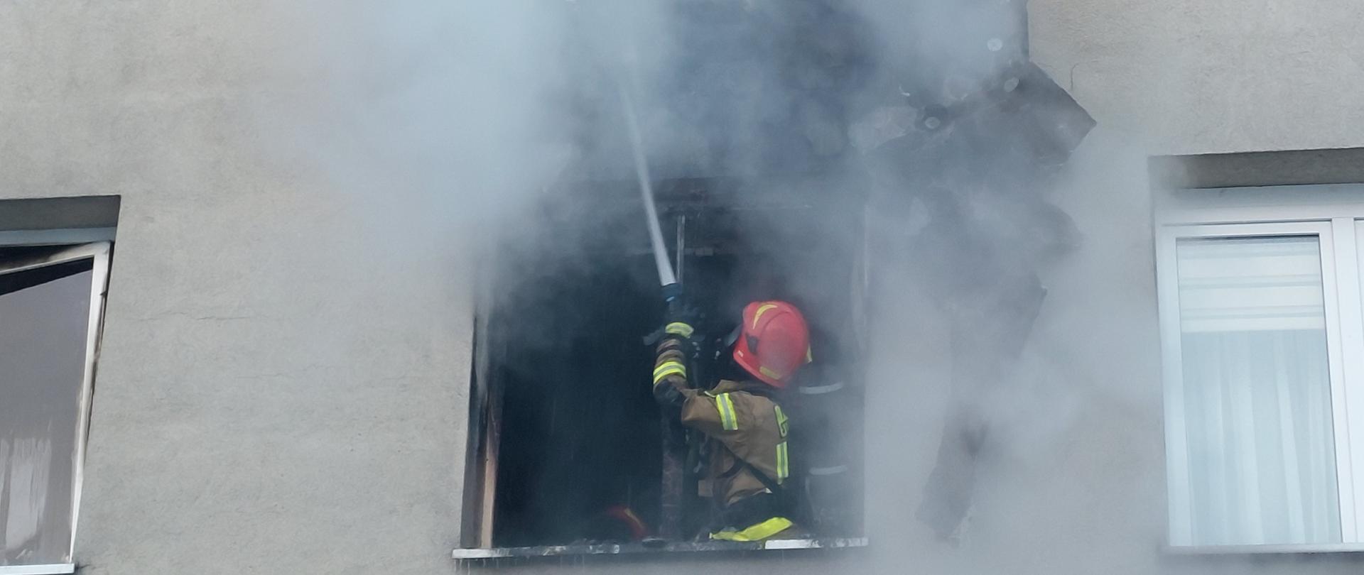 Strażak gasi wodą palącą się elewację nad wnęką okienną.