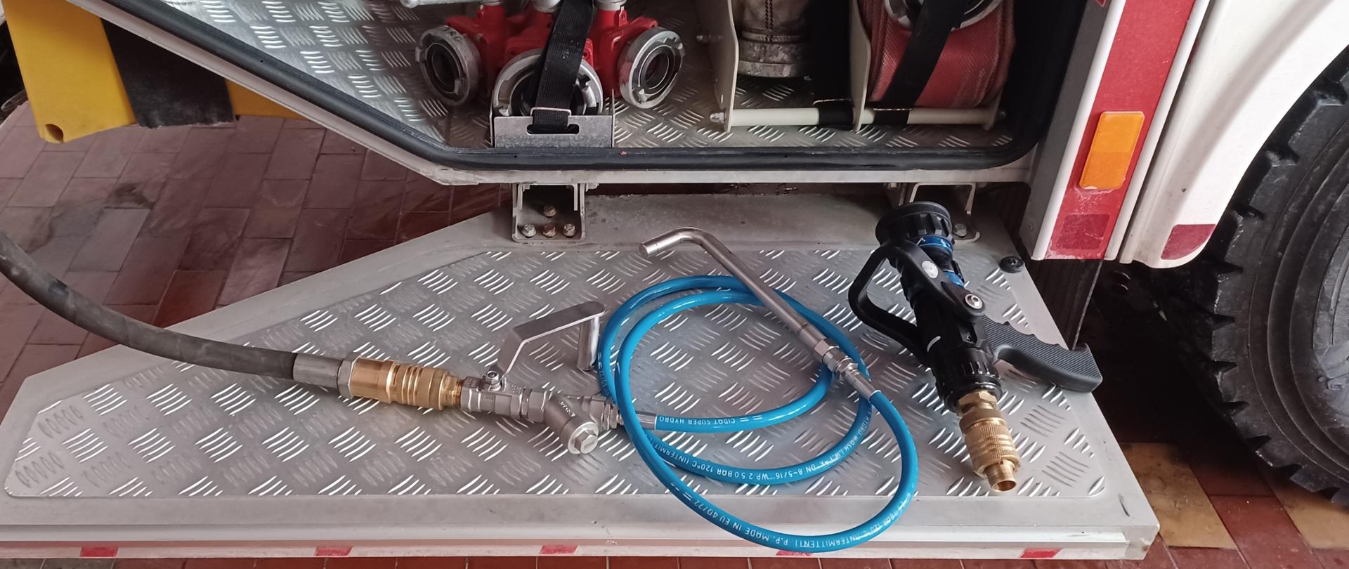 Zdjęcie przedstawia otwarty podest samochodu pożarniczego, którym leżą prądownica i podłączona do linii szybkiego natarcia lanca kominowa. W tle widać wyposażenie zamontowane w samochodzie pożarniczym tj. rozdzielacze, węże.