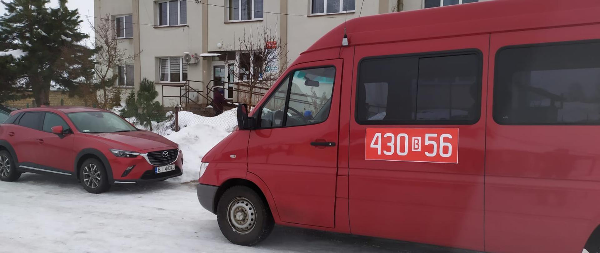Przed budynkiem ośrodka zdrowia w Narwi na zaśnieżonej drodze stoi strażacki czerwony bus z numerami operacyjnymi 430 b 56.