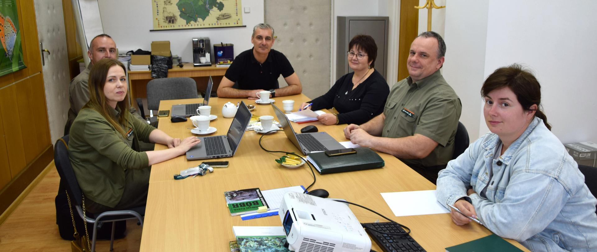Grupa sześciu osób (trzy kobiety i trzech mężczyzn) siedzi na krzesłach za stołem.