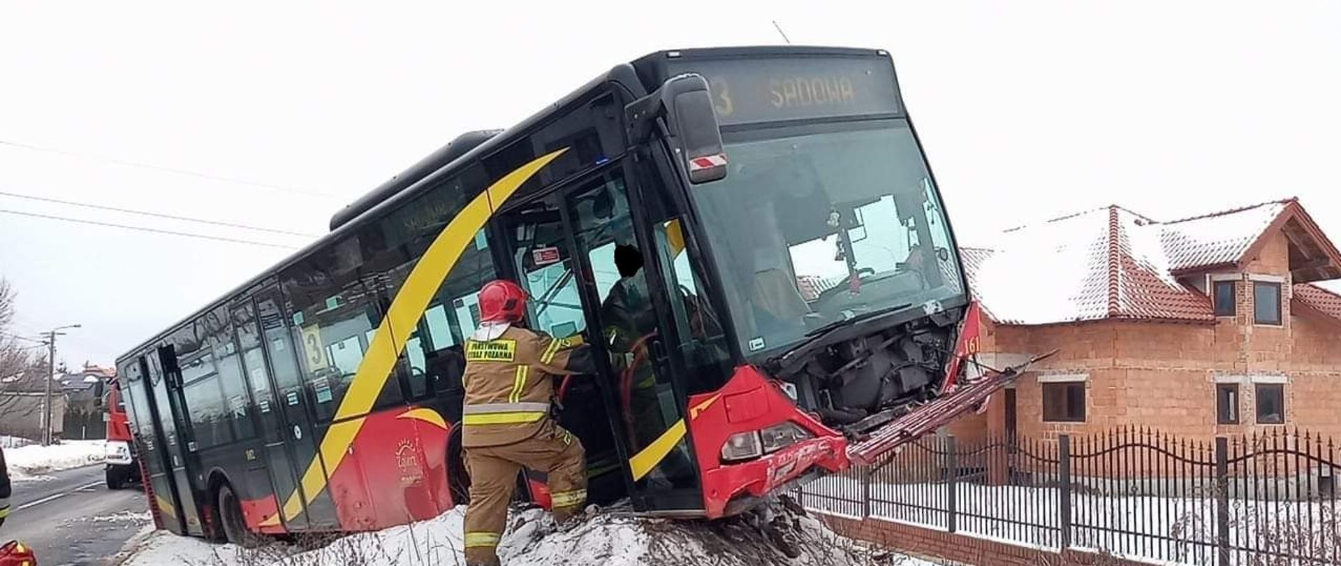 Na zdjęciu widać autobus który wypadł z drogi i wjechał na górę piachy na poboczu. Przy autobusie widać strażaka który pomaga wysiąść podróżującym.