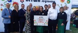Przedstawicielki Koła Gospodyń z voucherem na 5 tysięcy złotych w otoczeniu organizatorów na tle białej ścianki z napisem Bitwa Regionów