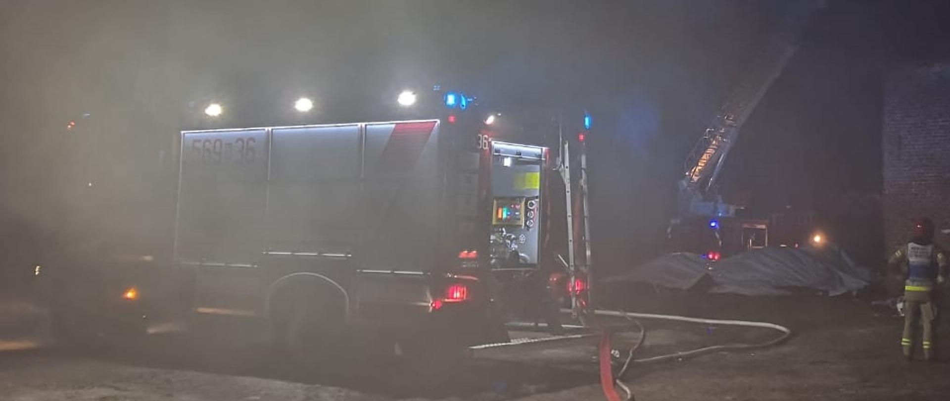 Pora nocna. Oświetlony samochód gaśniczy i SHD 23 stoją przy magazynie na zboże. Obok stoi KDR. 