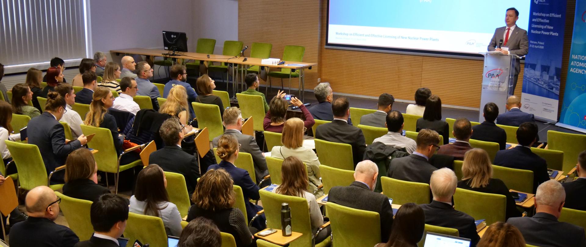 Prezes Państwowej Agencji Atomistyki otwiera warsztaty nt. licencjonowania obiektów jądrowych - prezes przemawia za pulpitem, uczestnicy siedzą na krzesłach i go słuchają 