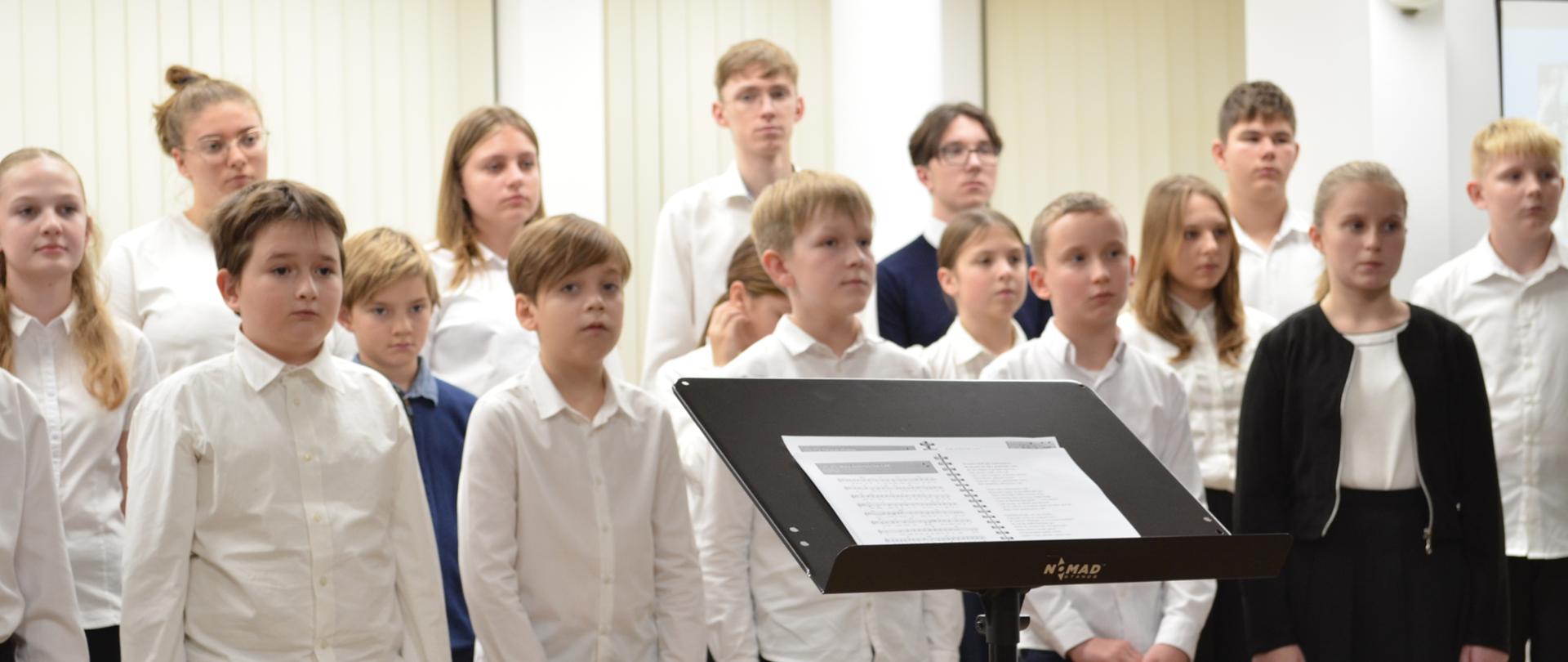 Chór szkoły muzycznej. Grupa chłopców i dziewcząt stoi w sali.