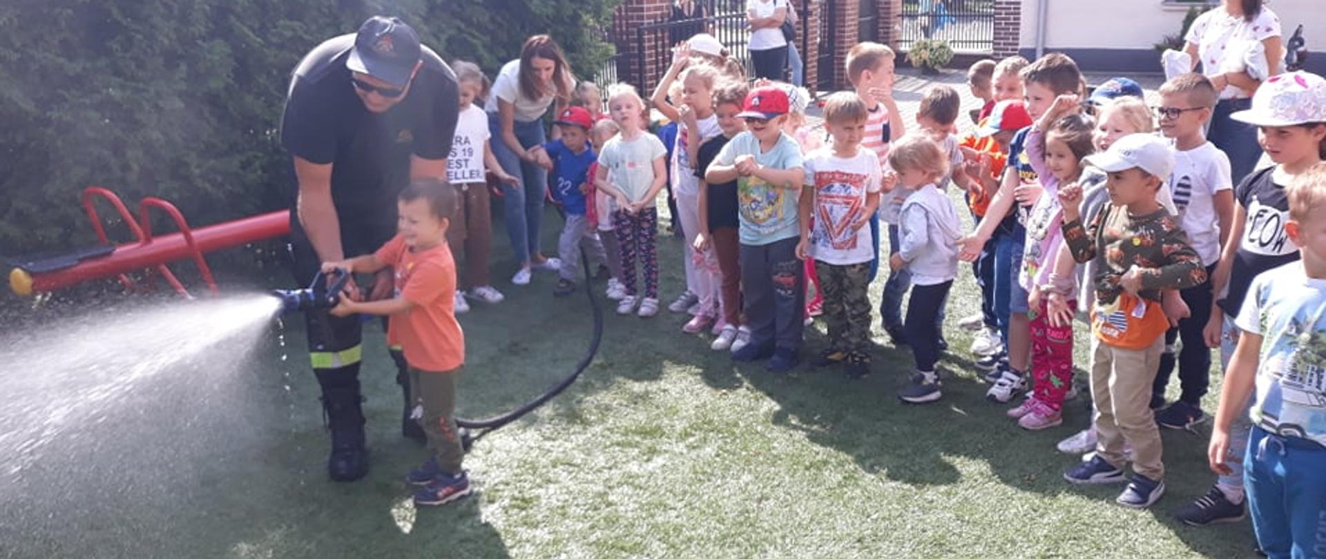 Zdjęcie przedstawia przedszkolaków i funkcjonariusza PSP pokazującego obsługę szybkiego natarcia