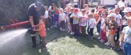 Zdjęcie przedstawia przedszkolaków i funkcjonariusza PSP pokazującego obsługę szybkiego natarcia