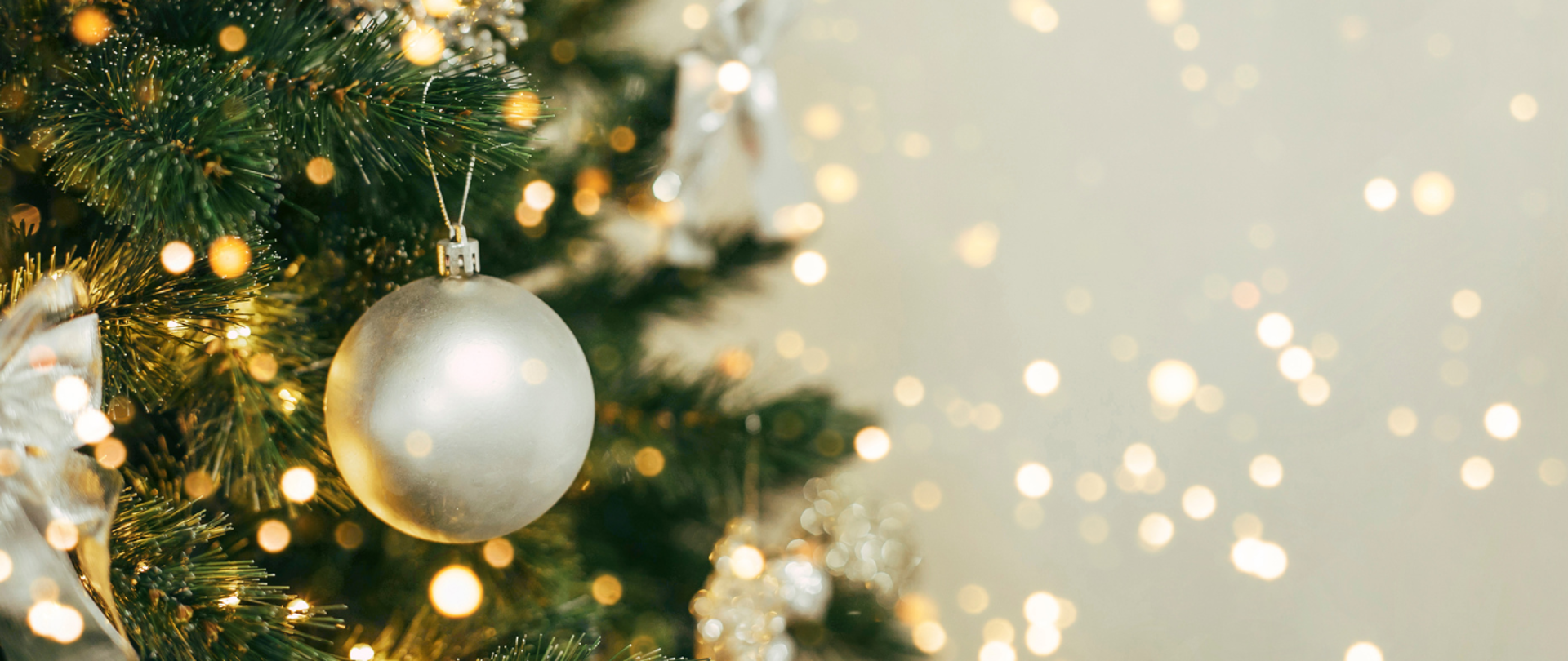 Fragment świątecznego drzewka z pojedynczą srebrną ozdobą, w tle jasne punkty światła.