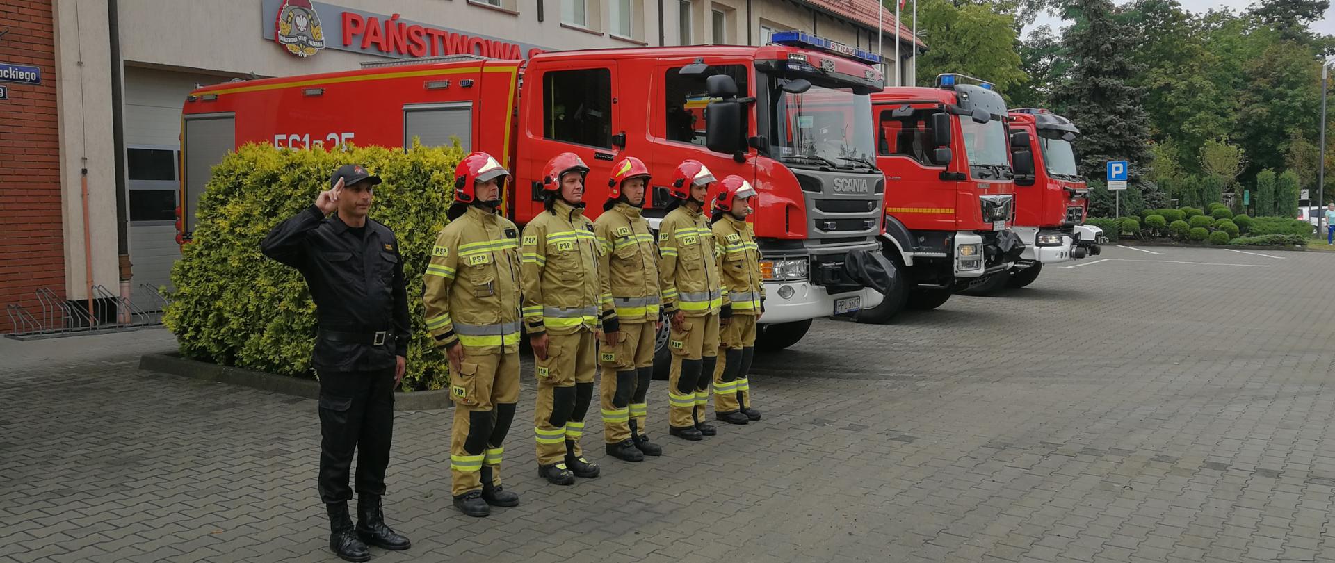 Na zdjęciu widać strażaków oddających honor bohaterom Powstania Warszawskiego przed Komendą Powiatową PSP w Pleszewie oraz stojącego obok samochody