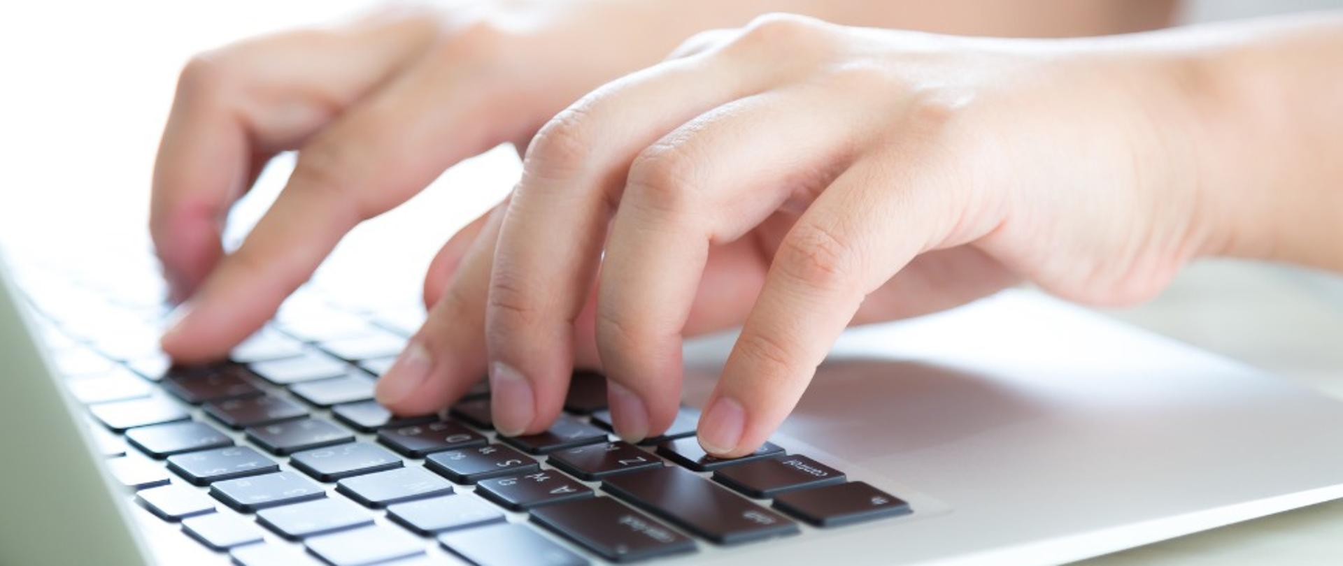 Grafika - palce stukające w klawiaturę laptopa.