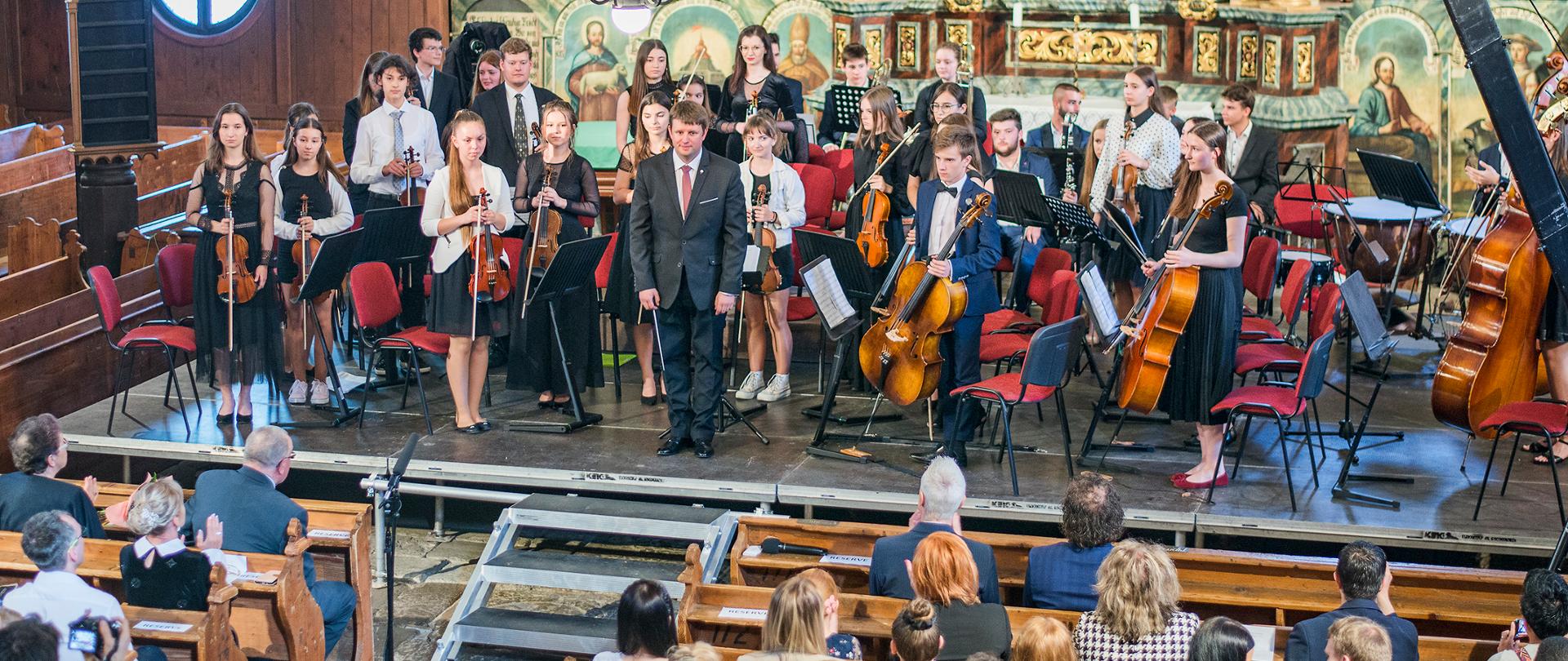 Zdjęcie przedstawia uczestników koncertu (uczniów ZPSM w Bochni) w drewnianym artykularnym kościele w Keżmarku na Słowacji.