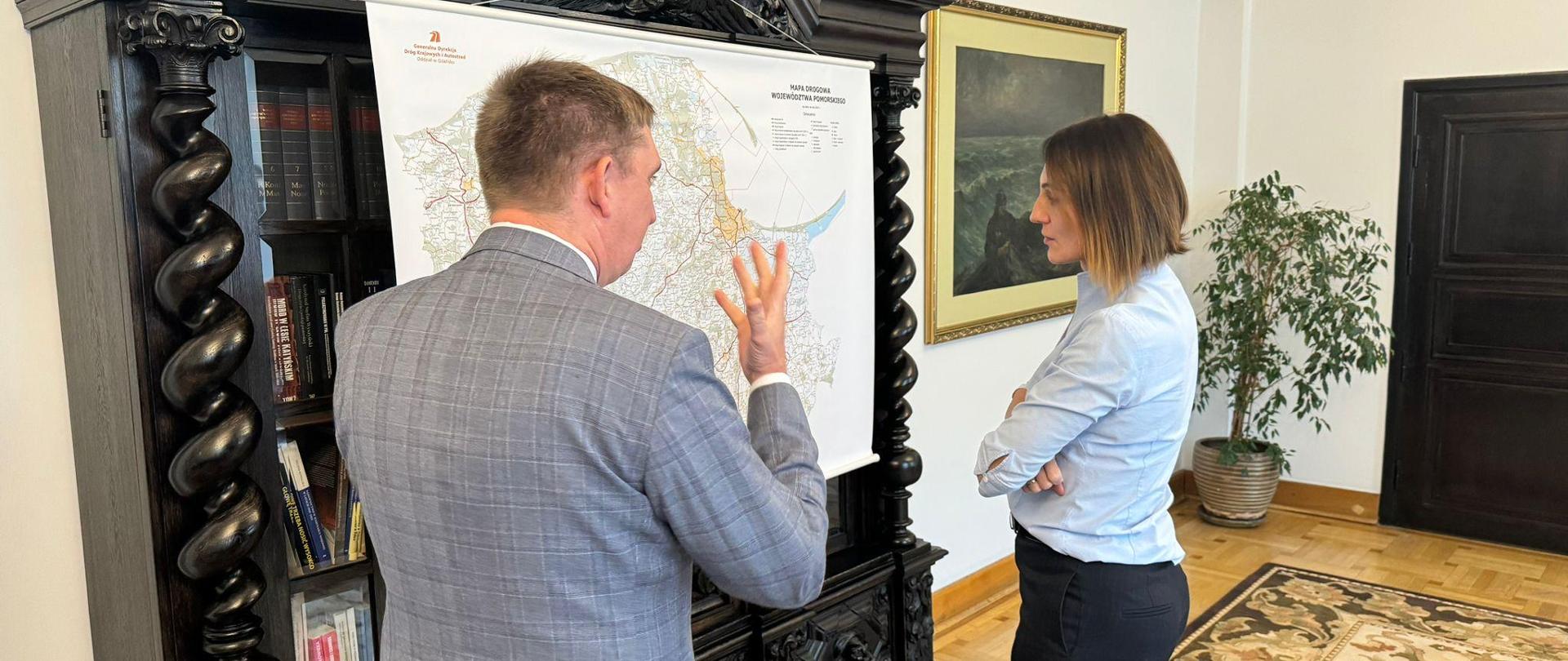 Mapa województwa z zaznaczonymi robotami drogowymi, przed nią stoi kobieta( wojewoda) i mężczyzna (dyrektor GDDKiA oddziału gdańskiego) 