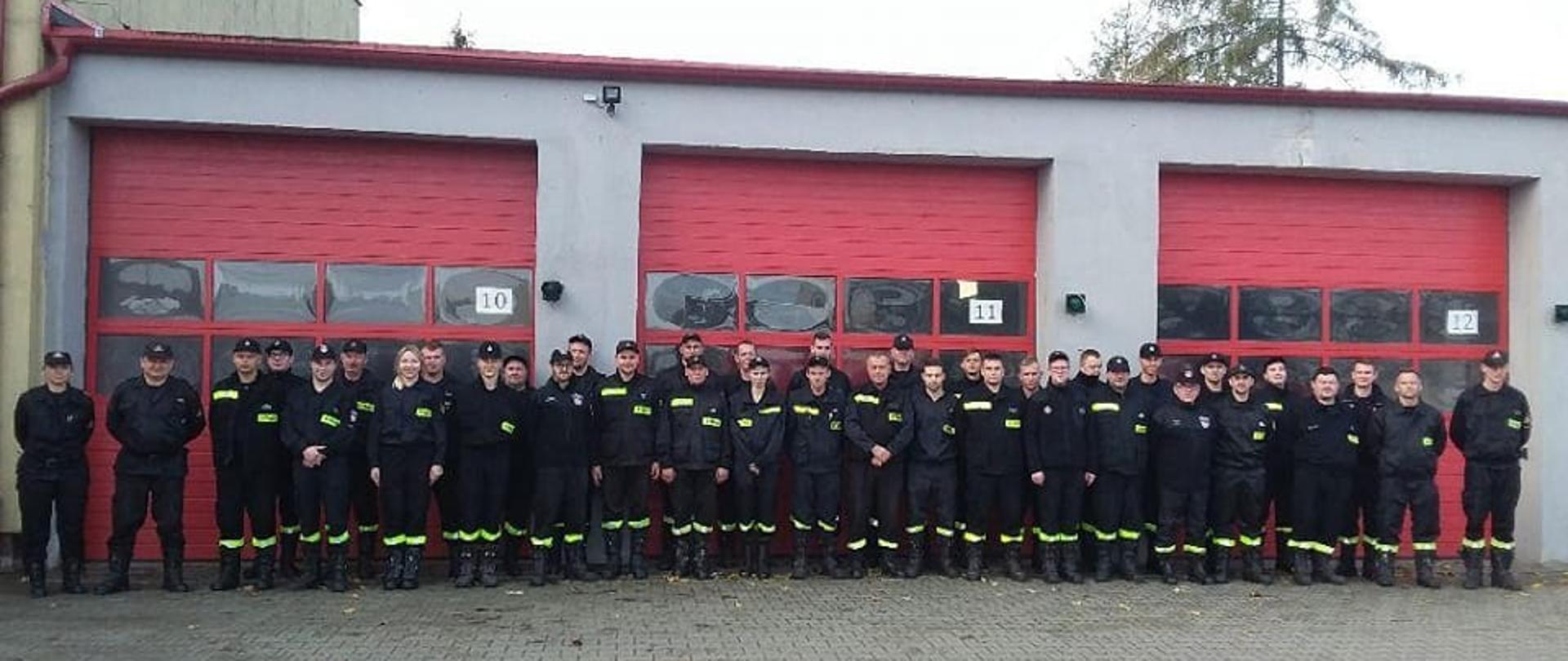 Uczestniczy egzaminu zgromadzeni w dwuszeregu przed bramami wjazdowymi do remizy.