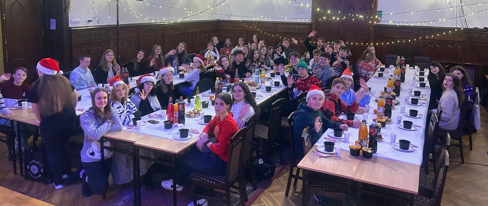 uczniowie szkoły zgromadzeni przy trzech długich stołach na sali królewskiej podczas wigilii zorganizowanej przez Samorząd Uczniowski 