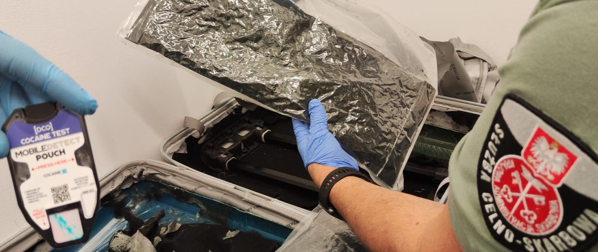 Ramię funkcjonariusza Służby Celno-Skarbowej, trzyma narkotyki, które były ukryte w ściankach walizki.