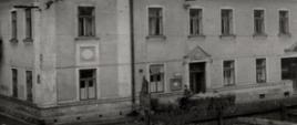 Zdjęcie czarno białe przedstawia stary budynek szkoły muzycznej kamienicę, przed którą przejeżdża woźnica. 