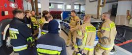 Grupa strażaków Ochotniczej Straży Pożarnej podczas praktycznego pokazu samochodu hybrydowego typu plug-in (PHEV). W tym w przypadku jest to oznakowany radiowóz Policji.