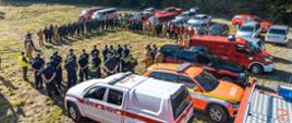 Grupowe zdjęcie podczas przywitania uczestników ćwiczeń i obserwatorów w Jarnołtówku. Za osobami znajdują się samochody straży pożarnej z Polski i Czech.