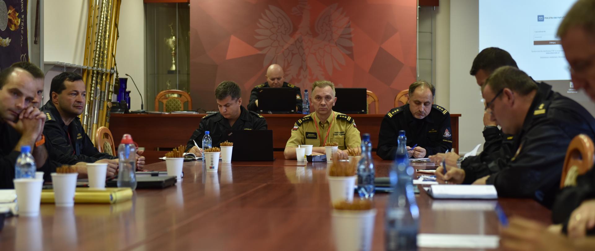 strażacy siedzący przy stolach w czasie odprawy