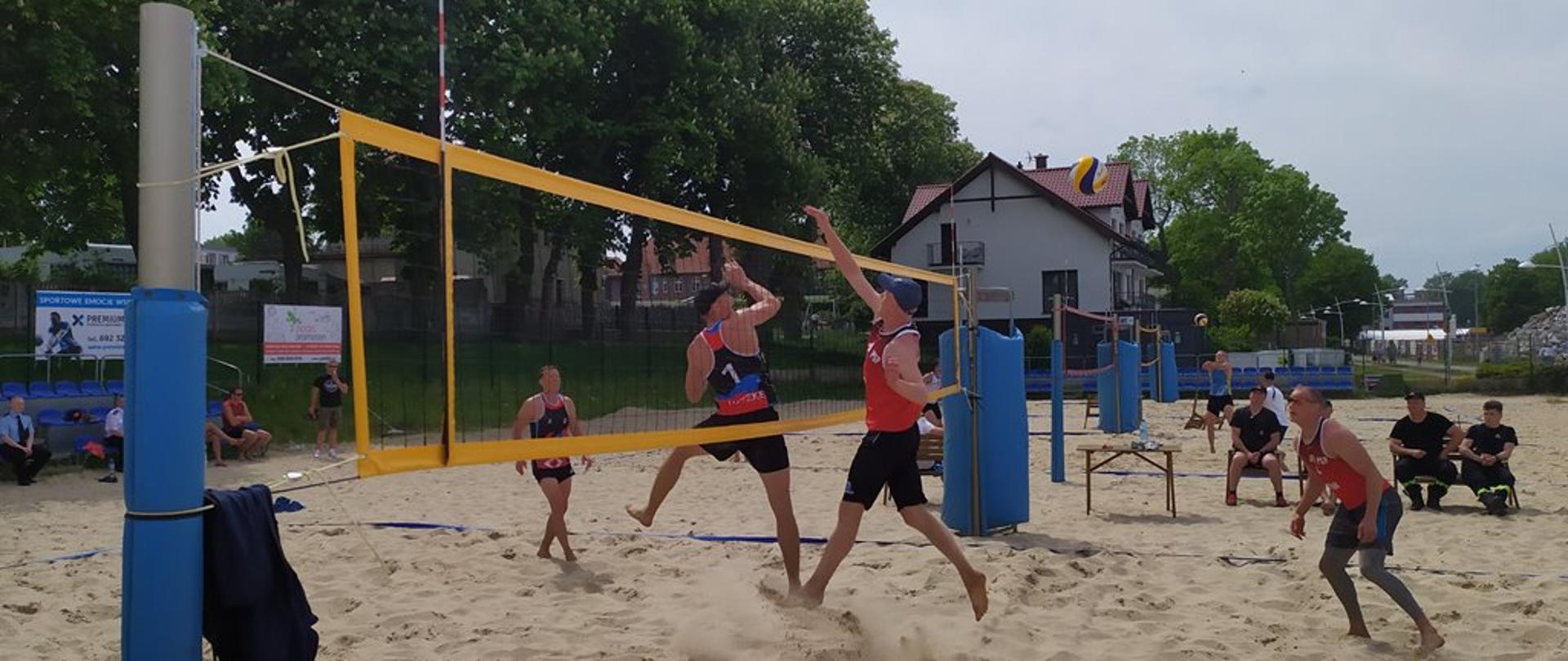 Zawodnicy rozgrywający mecz siatkówki plażowej.