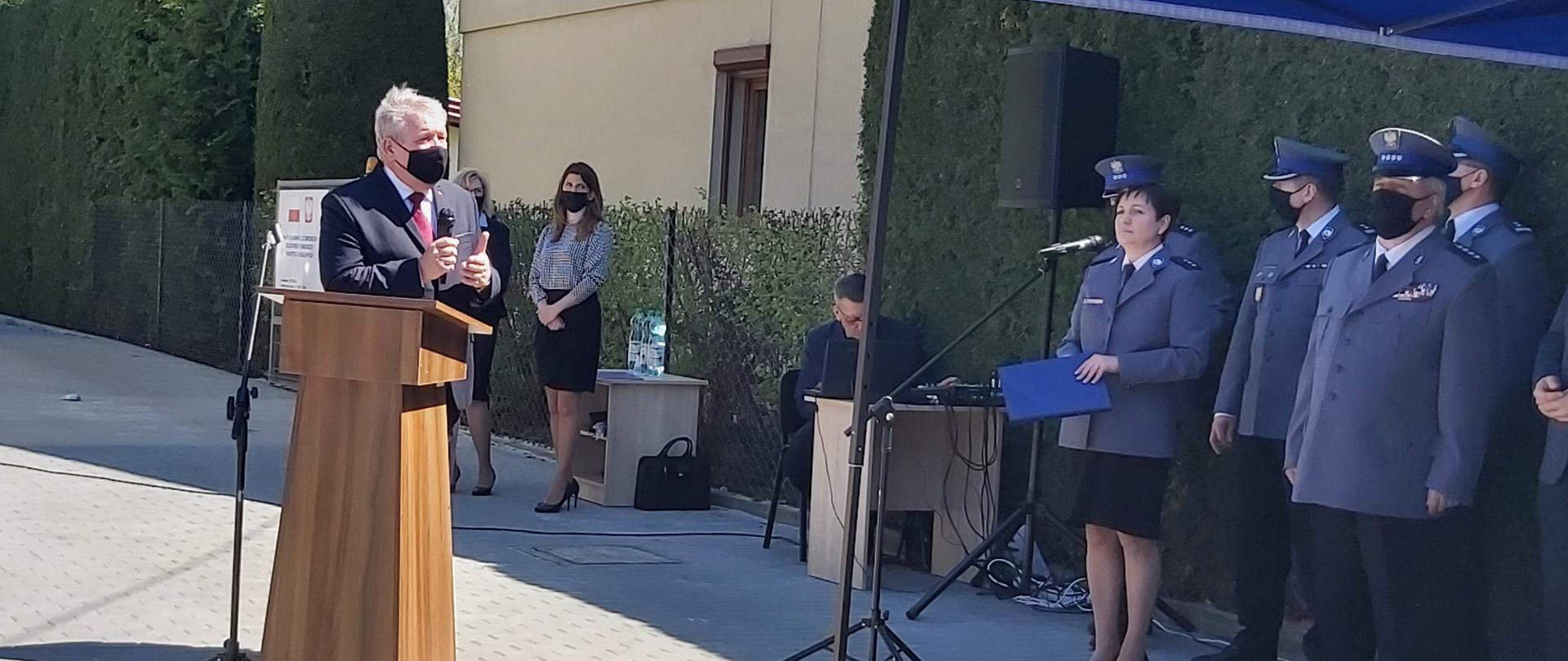 Na zdjęciu po prawej stronie znajduje się kilku policjantów, po lewej mężczyzna przemawiający z mównicy