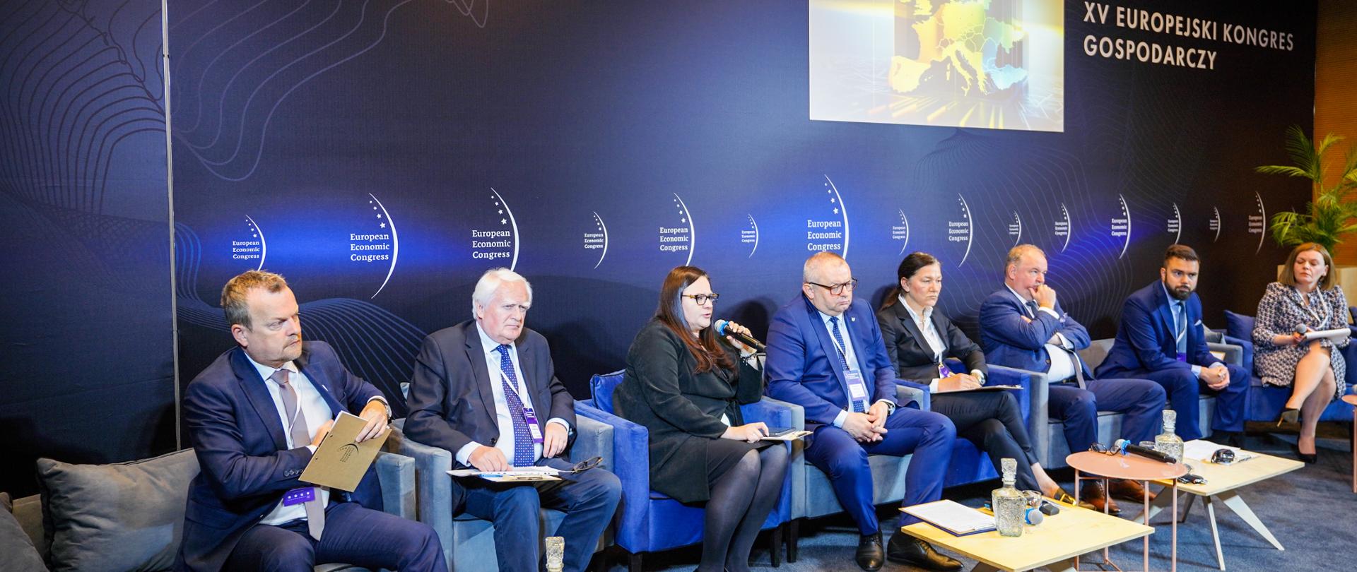 W sali konferencyjnej grupa osób siedzi w fotelach przed stolikami. Wiceminister Małgorzata Jarosińska-Jedynak z mikrofonem.