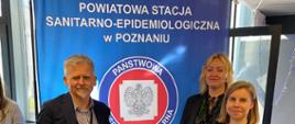 Trzech pracowników Powiatowej Stacji Sanitarno-Epidemiologicznej na tle baneru Stacji PSSE w Poznaniu
