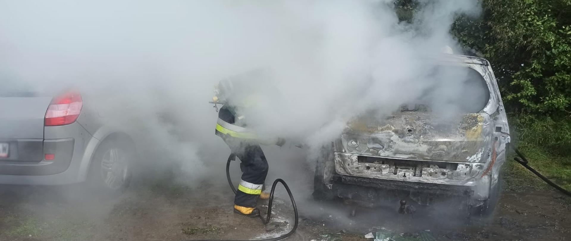 Strażak gasi samochód z którego wydobywa się dym.