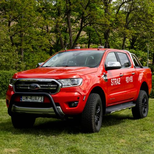 Czerwony, uterenowiony pickup Ford Ranger z podwójną kabiną i czarnym orurowaniem z przodu (bullbar). Na przednich drzwiach umieszczono biały napis „STRAŻ” a na tylnych numer operacyjny „401[D]90”. Pojazd ma terenowe opony, czarne felgi i stoi na zielonym trawniku.